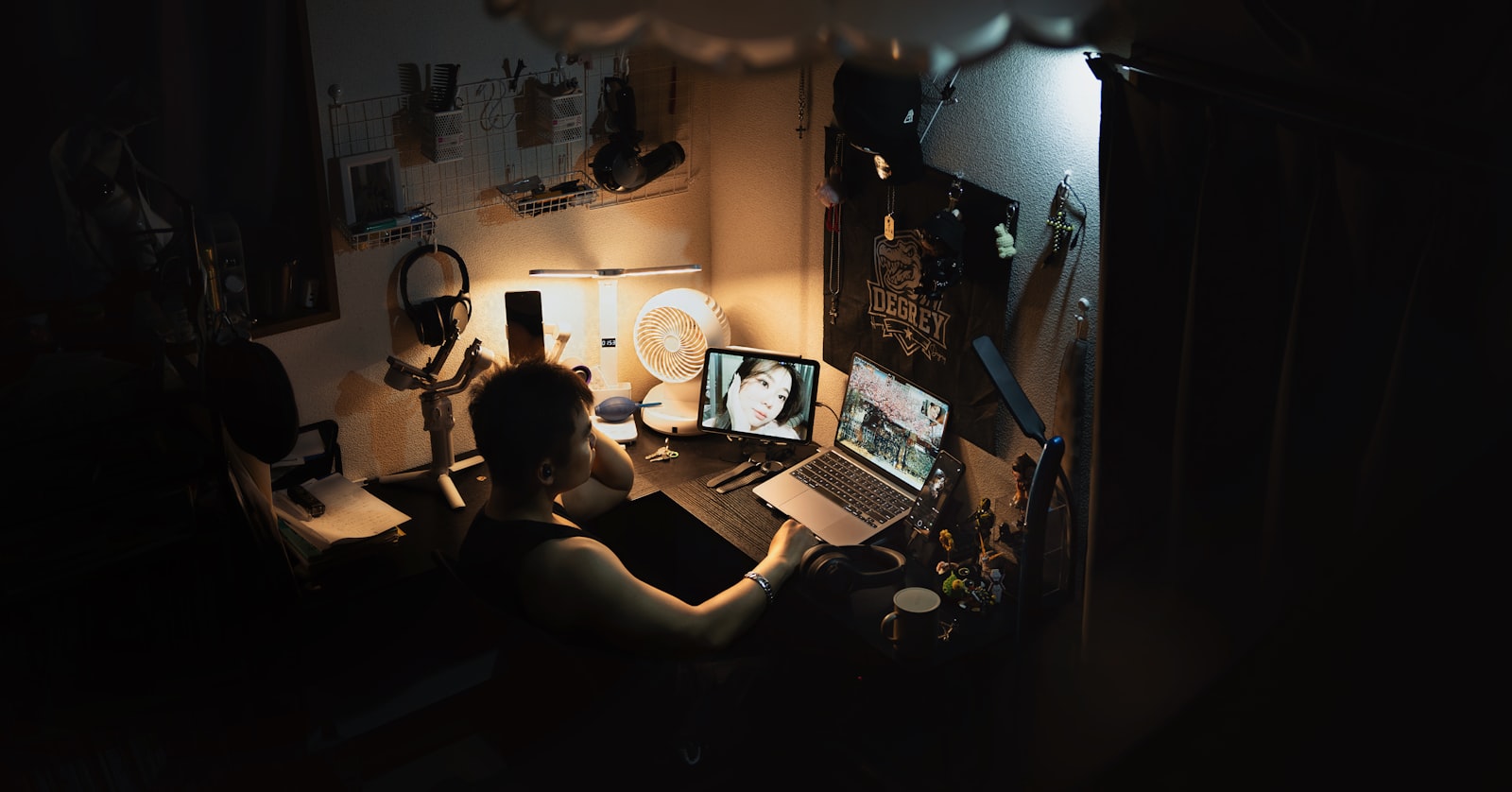 Pessoa usando notebook e celular sobre a mesa em um ambiente escuro