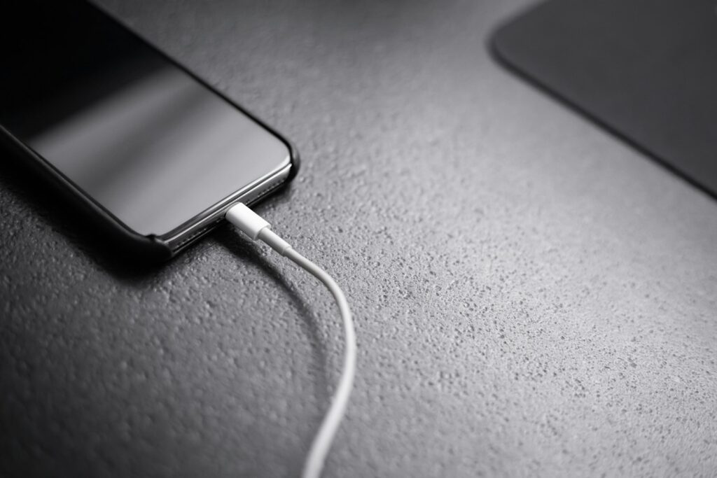 Smartphone preto carregando com cabo sobre uma mesa escura