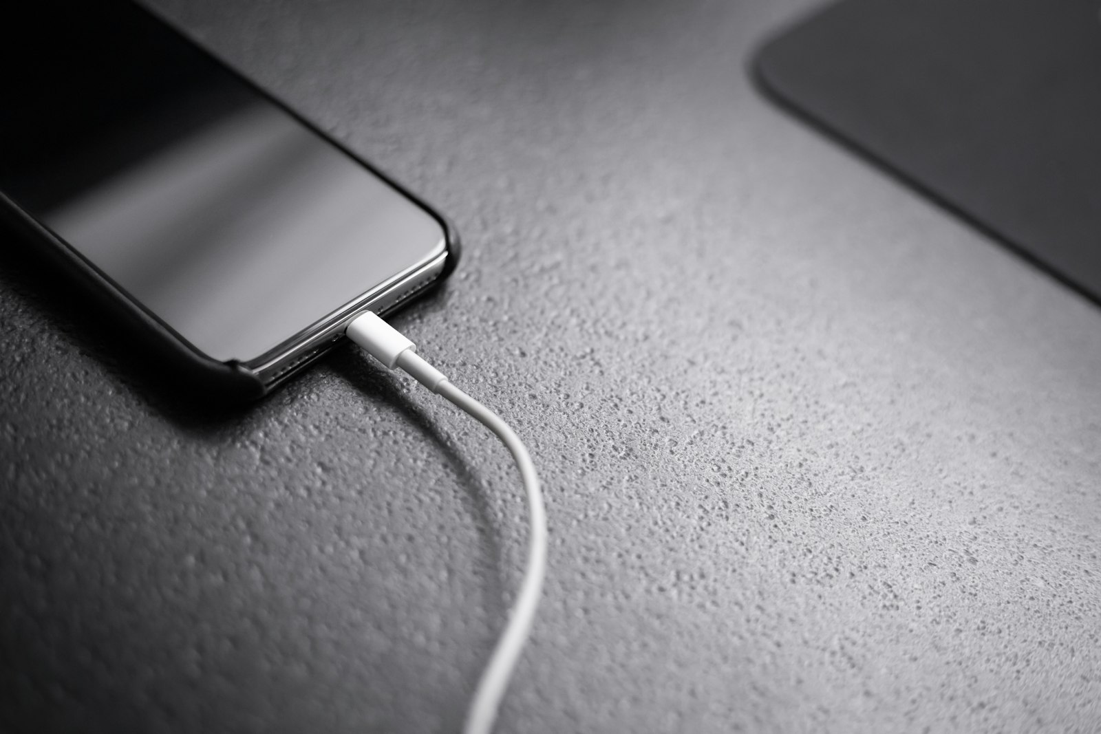 Celular preto conectado a um cabo de carregador sobre a mesa
