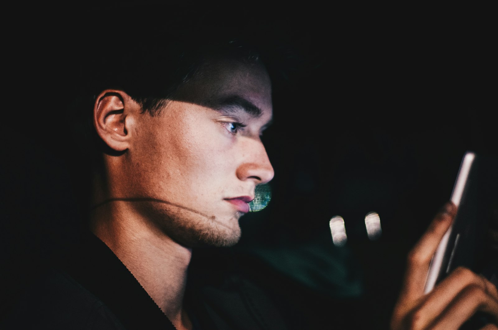 Homem de pé no escuro olhando a tela do celular à noite