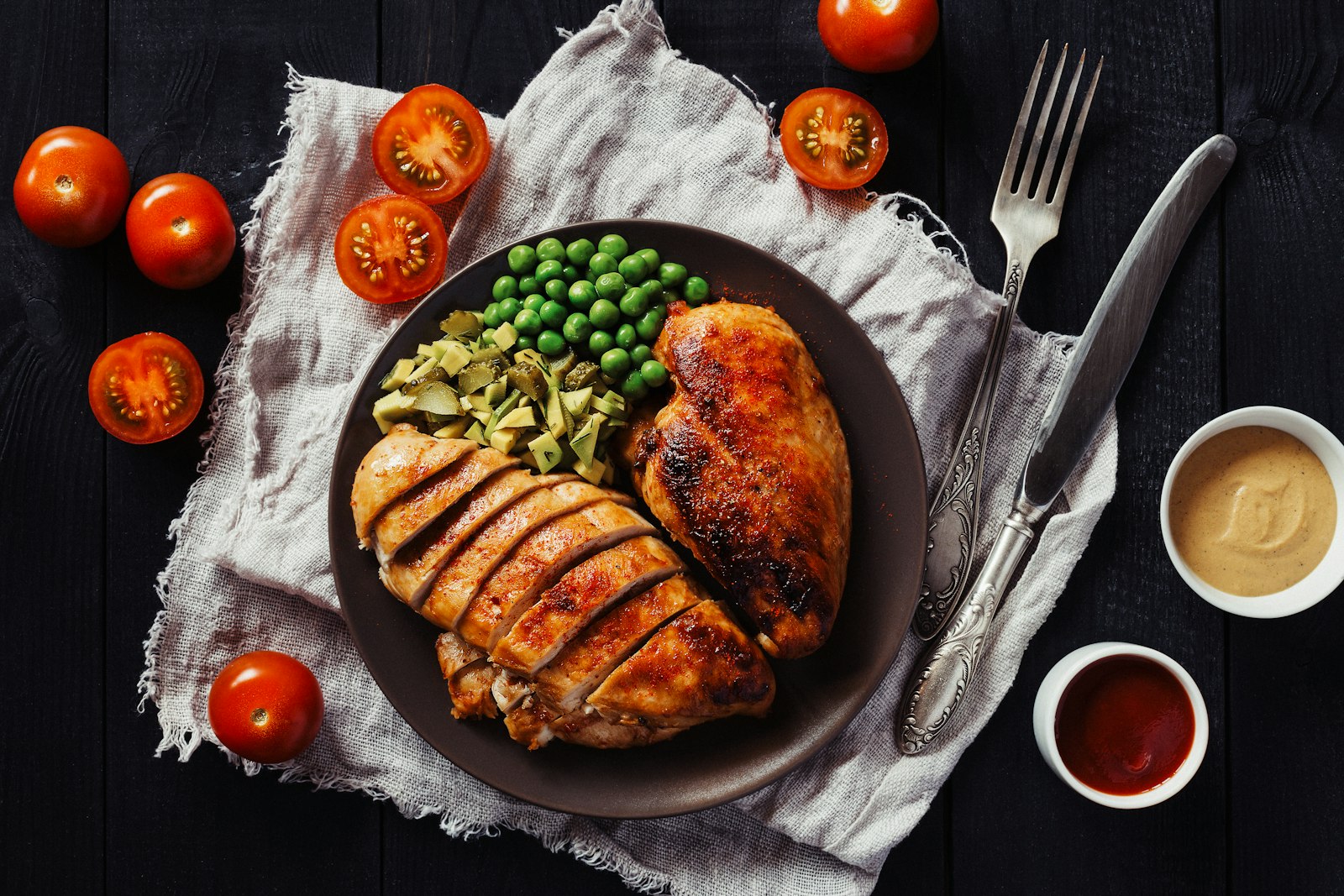 Peito de frango fatiado servido em um prato escuro com legumes