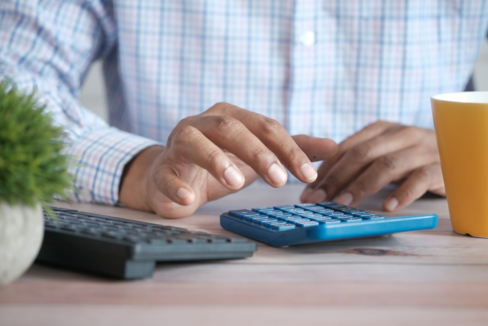Pessoa usando calculadora sobre a mesa com papéis e uma caneca de café