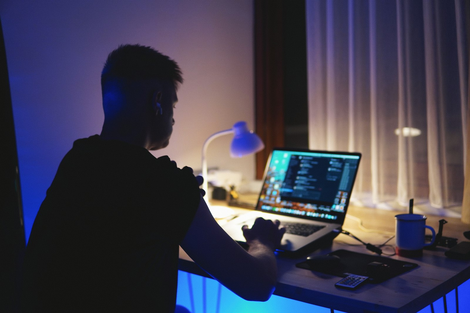 Homem sentado no escritorio de casa a noite usando o notebook