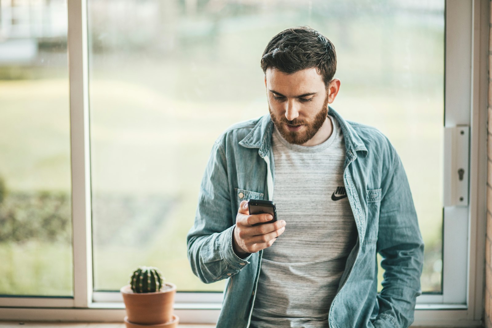 Homem de pé perto da janela usando o aplicativo do banco no celular