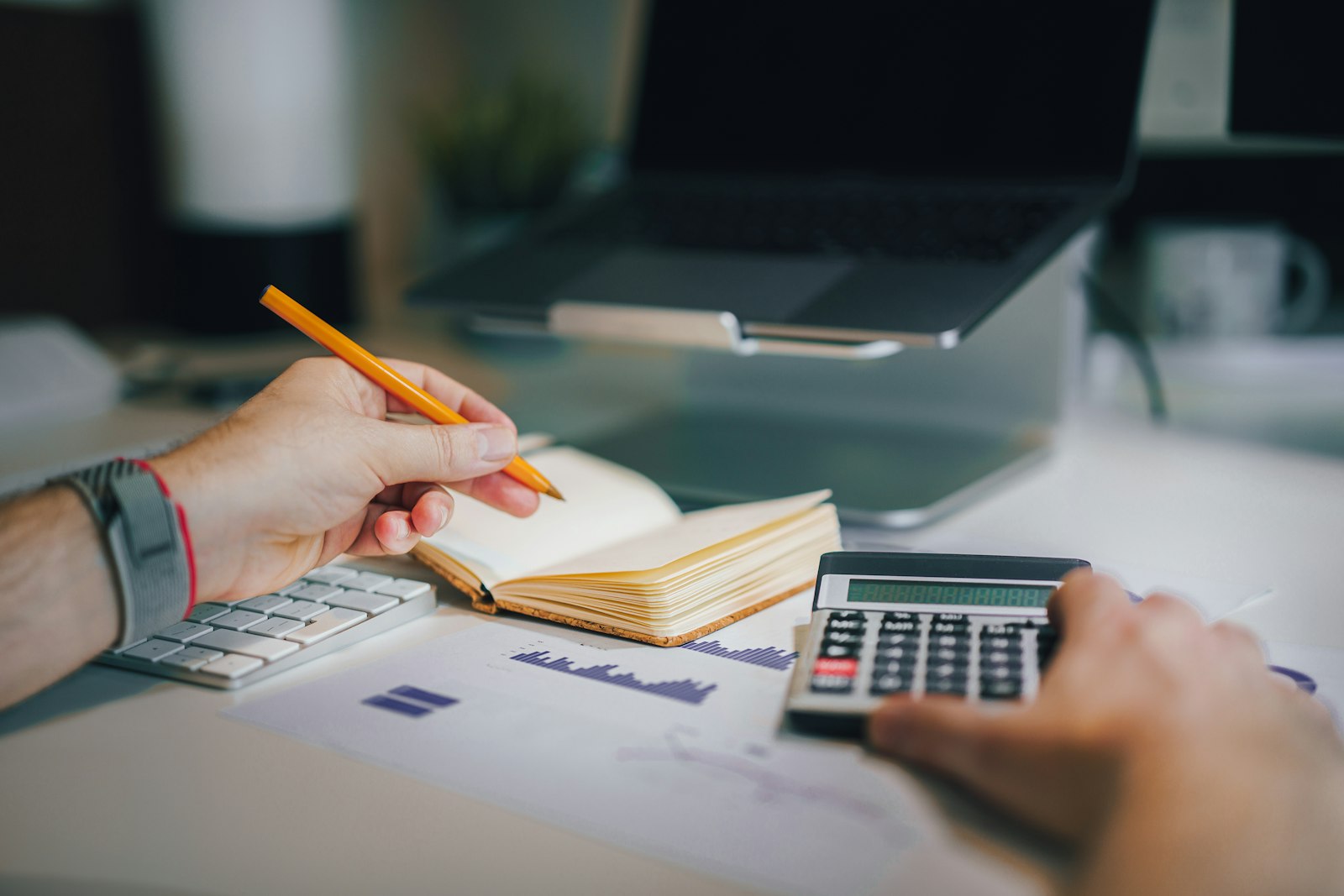 Pessoa sentada à mesa com calculadora e caderno fazendo contas