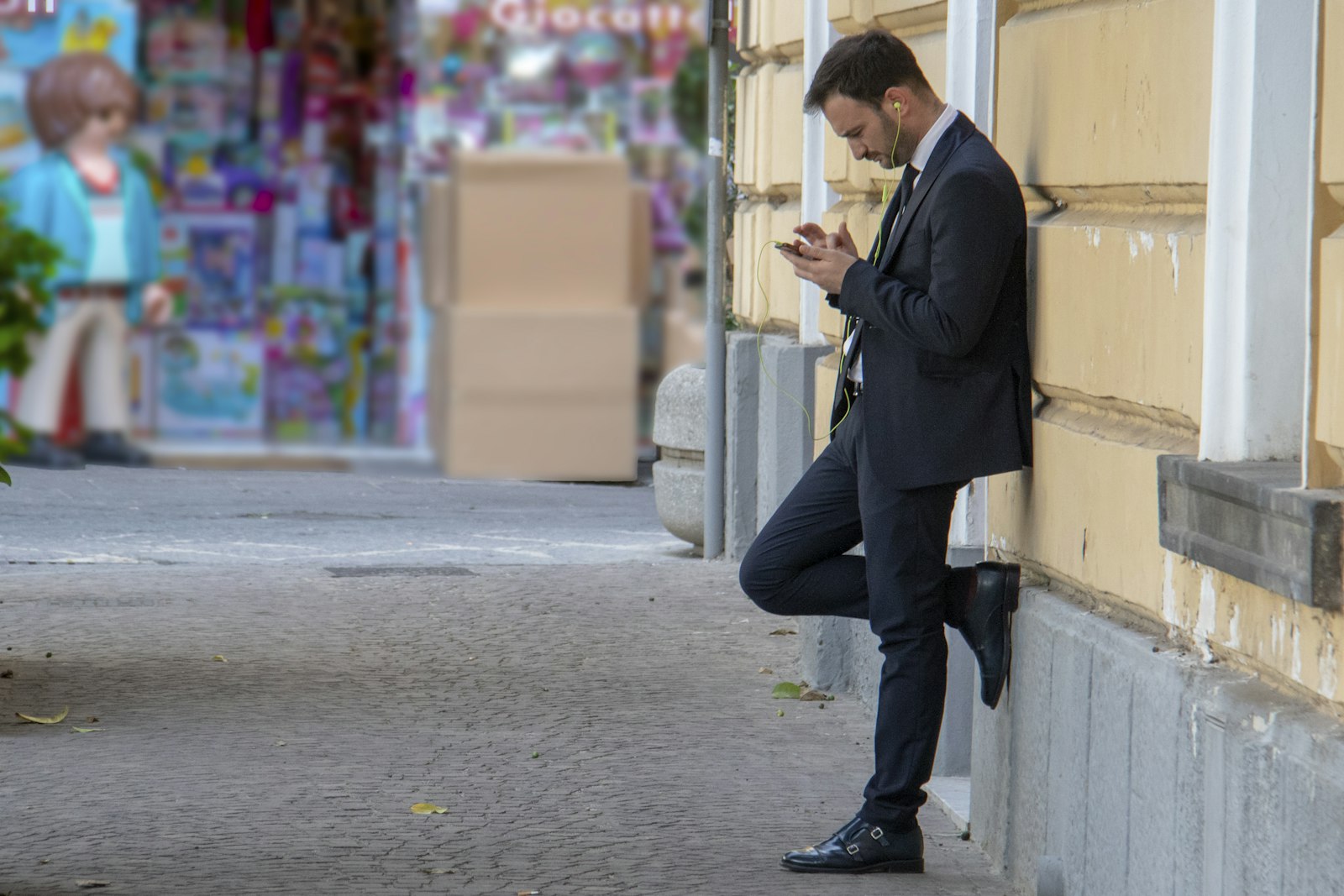 Homem encostado em um prédio olhando o celular na rua