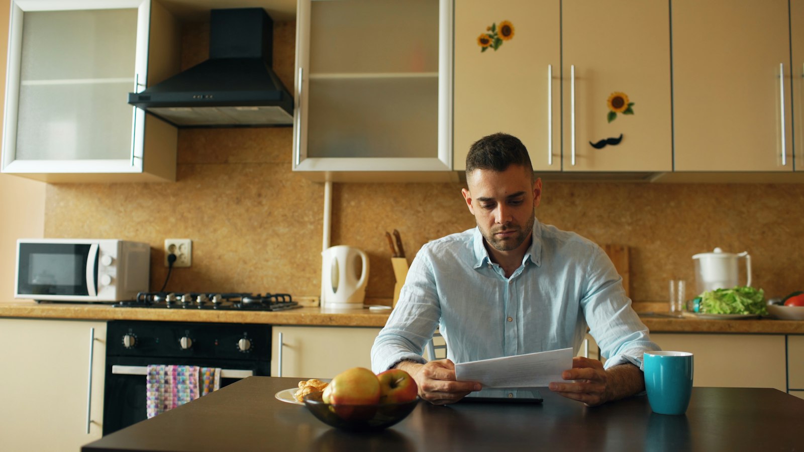 Homem lendo um documento sentado à mesa da cozinha com uma caneca de café