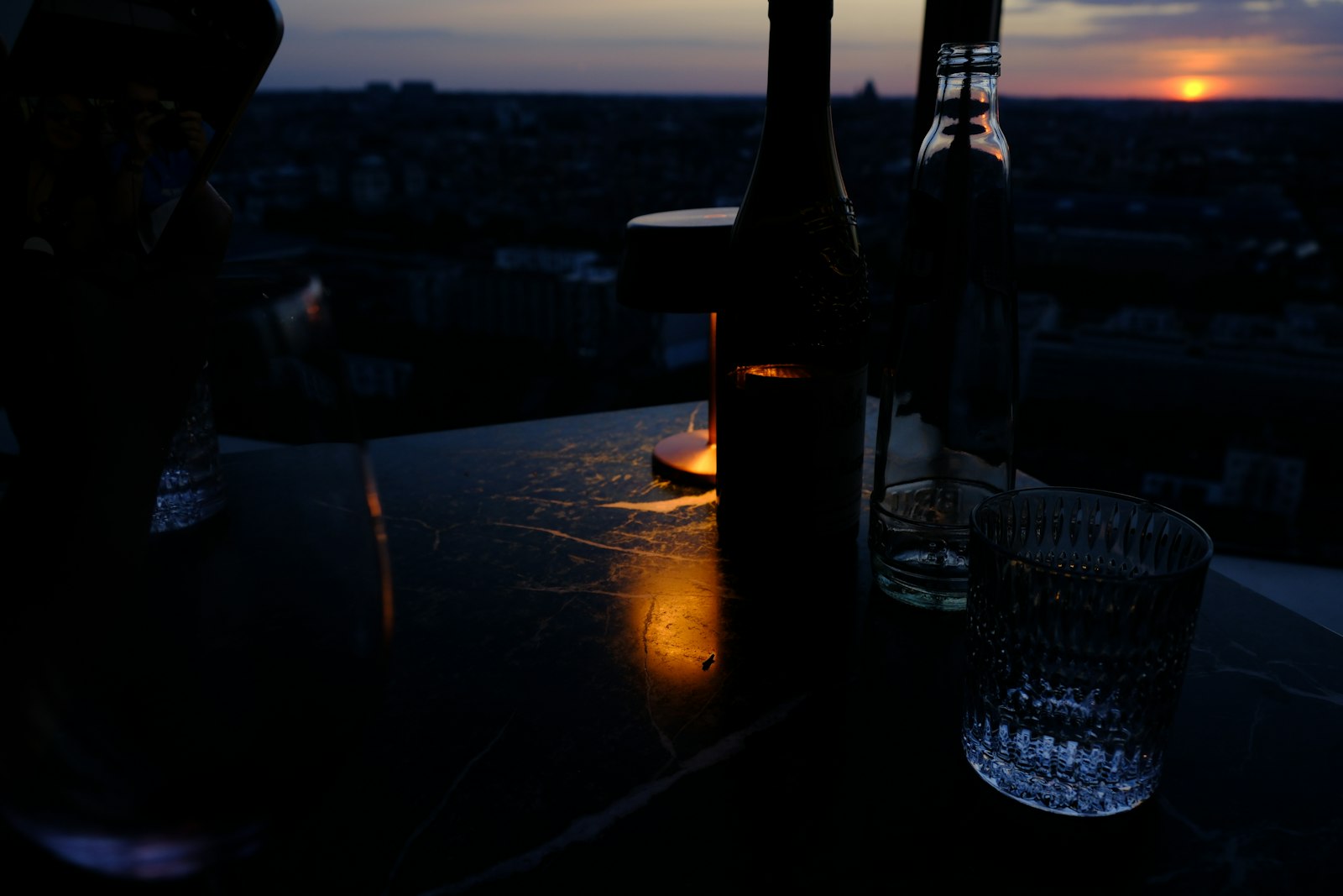 Garrafa e copo sobre uma mesa escura em ambiente de pouca luz