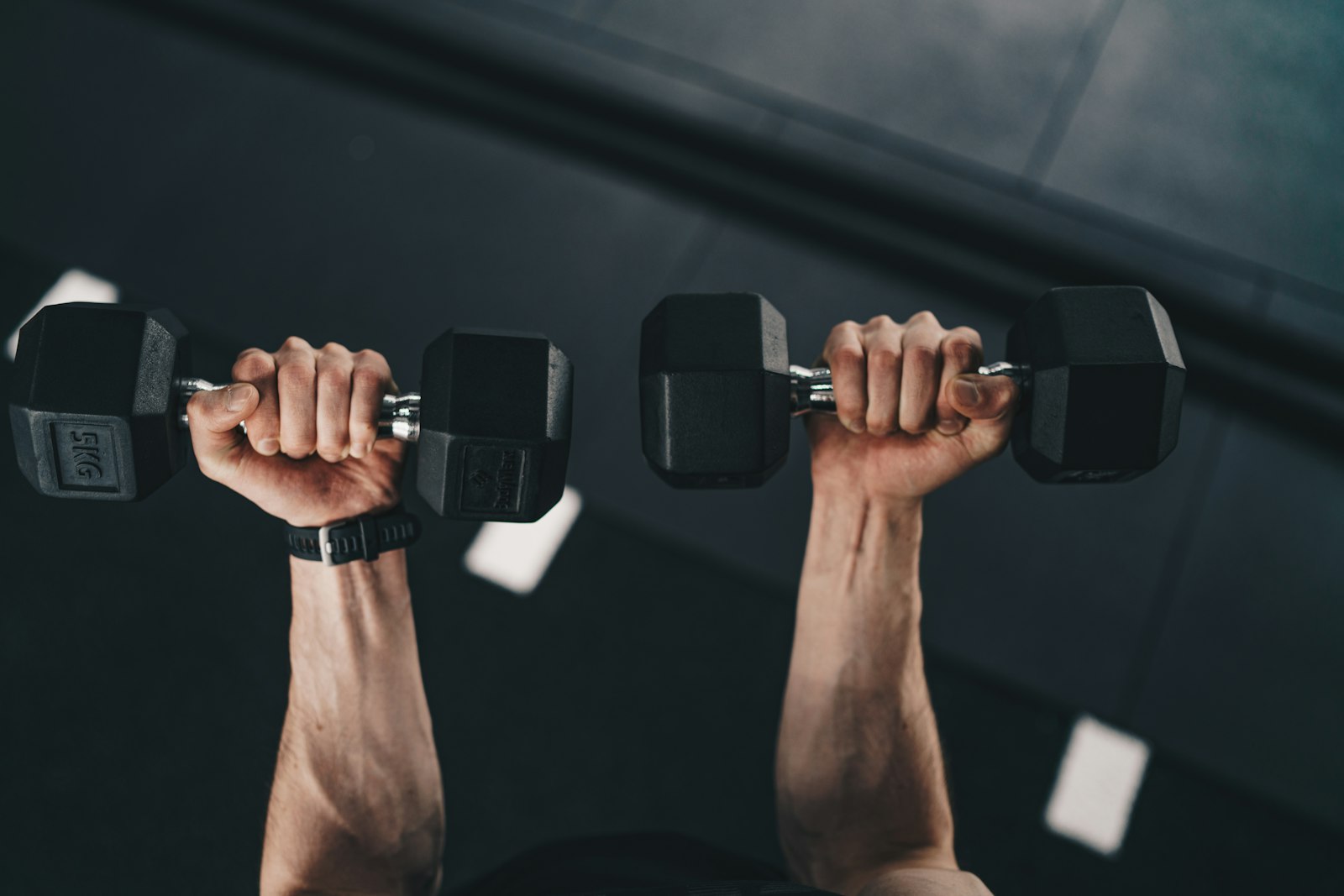 Homem levantando dois halteres durante o treino na academia