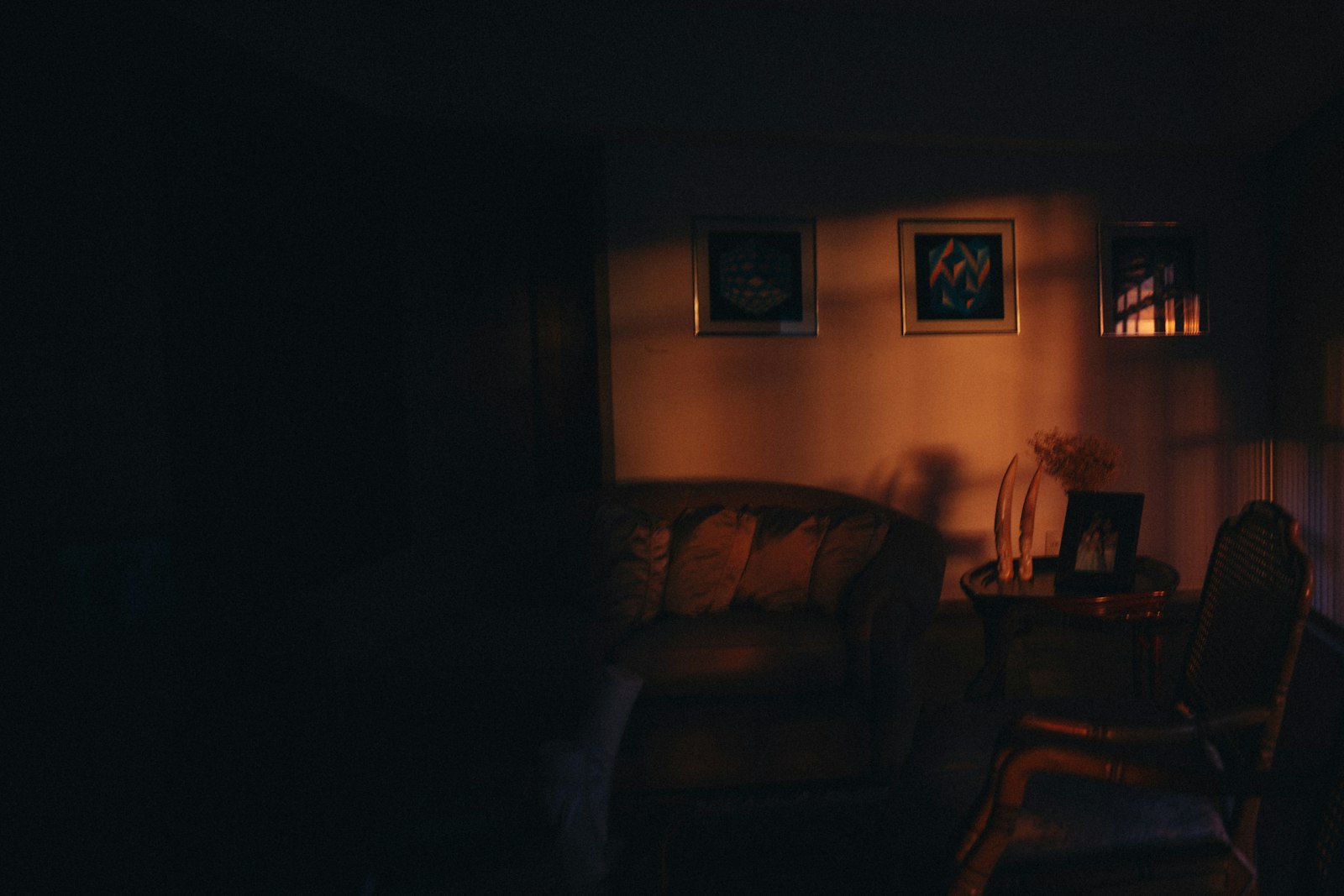 Sala de estar à noite iluminada por uma única luminária, com sofá e quadros na parede