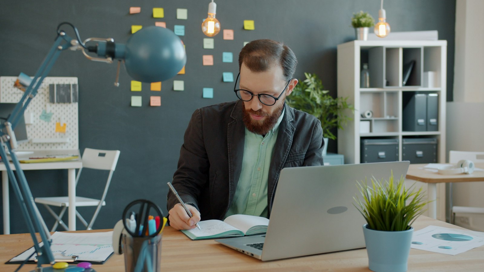 Homem sentado a mesa com notebook e caderno fazendo contas