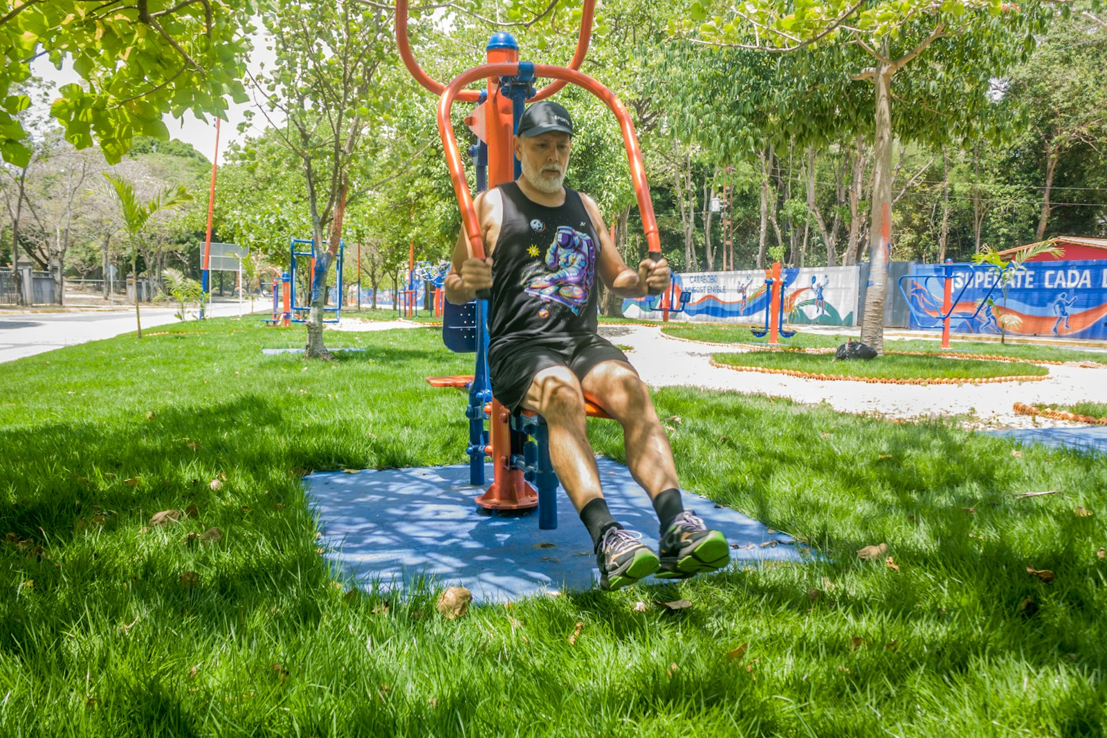 Homem mais velho de barba grisalha treinando num aparelho de academia ao ar livre num parque