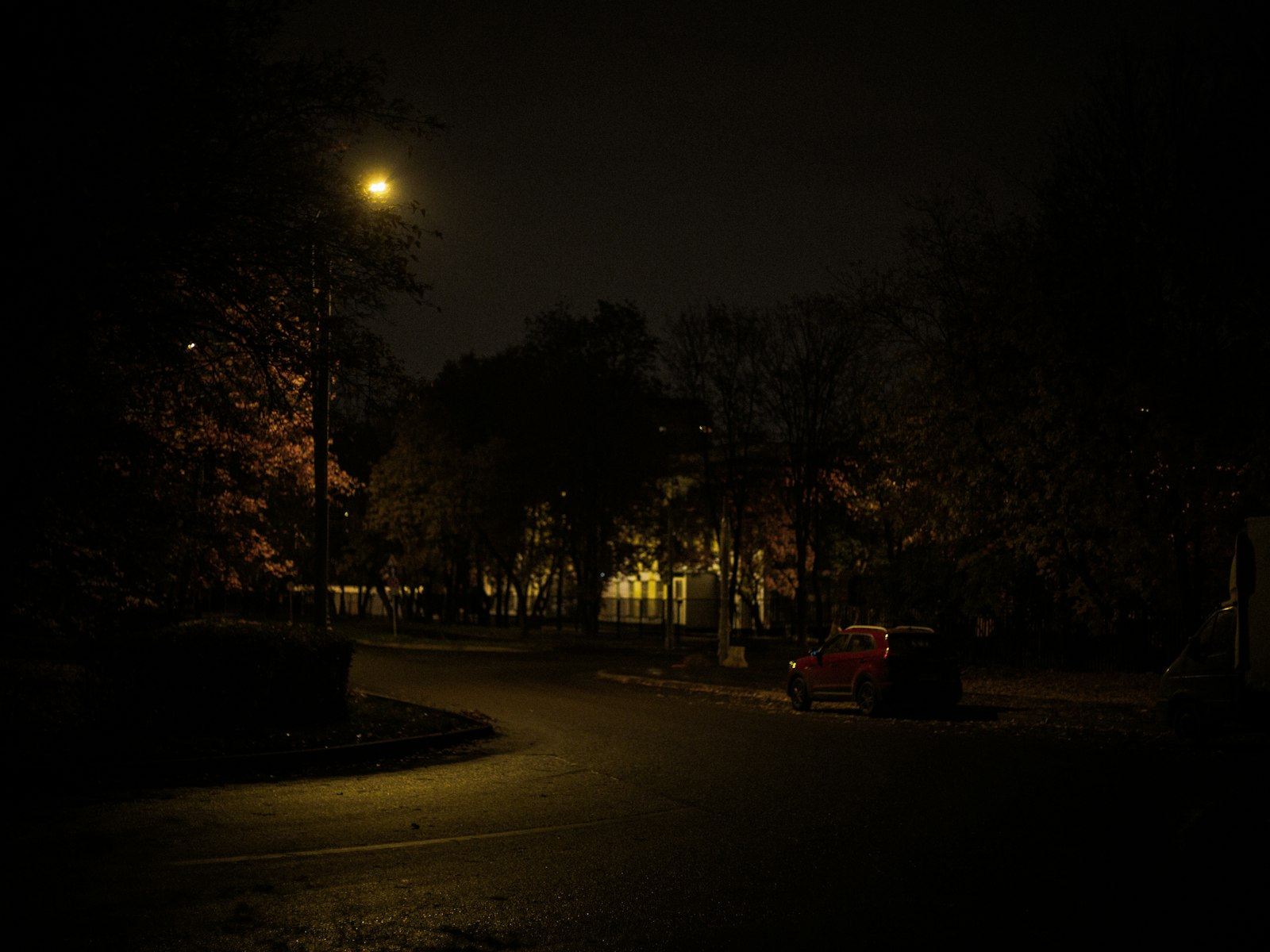 Rua residencial escura iluminada por um poste a noite, onde os carros ficam estacionados
