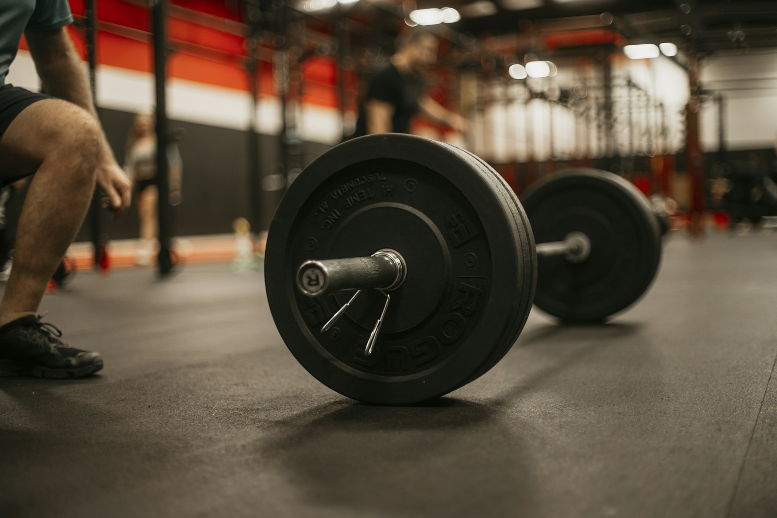 Homem agachado ao lado de uma barra de musculação na academia