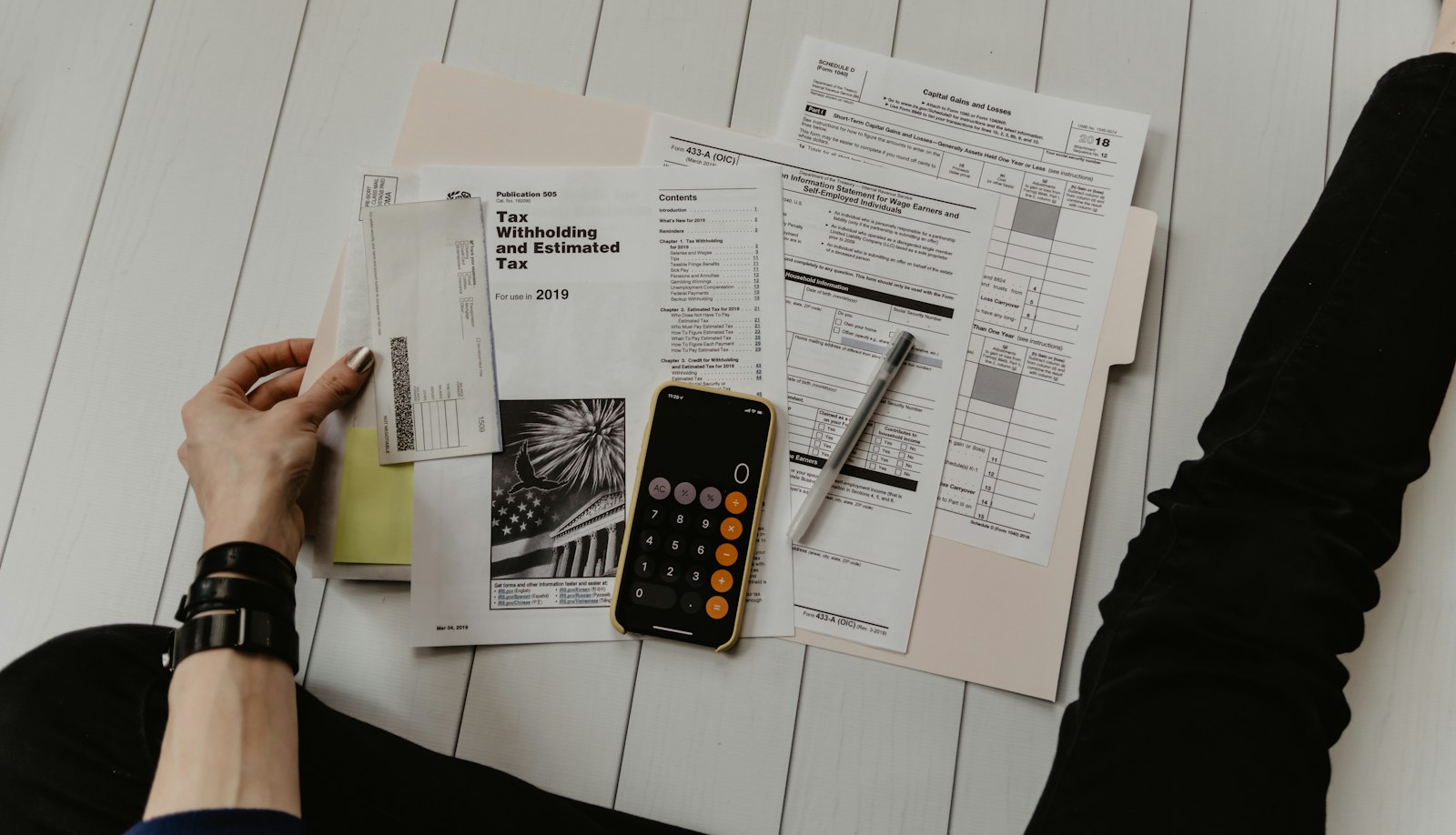 Maos com papel caneta e calculadora fazendo contas sobre a mesa