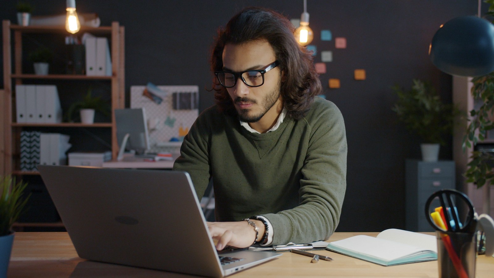 Homem de oculos trabalhando em um notebook em escritorio a noite