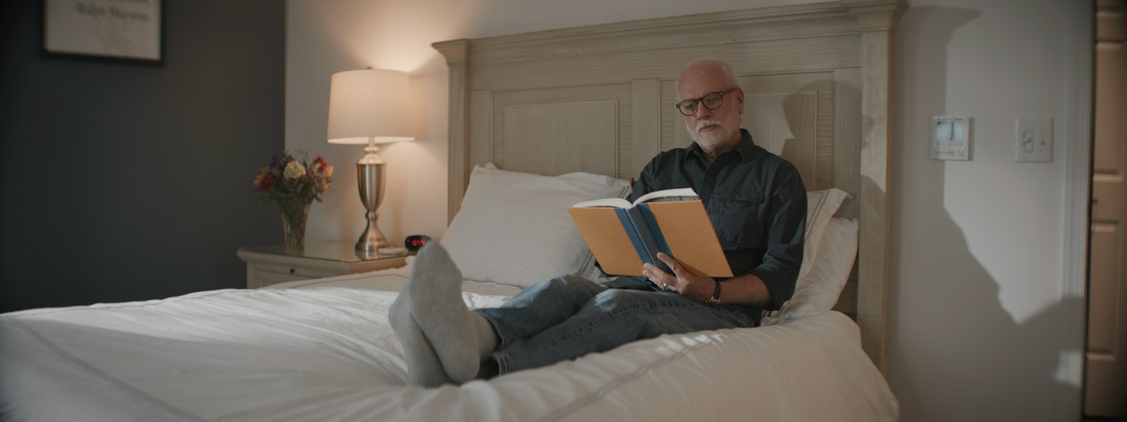 Homem deitado na cama lendo um livro impresso